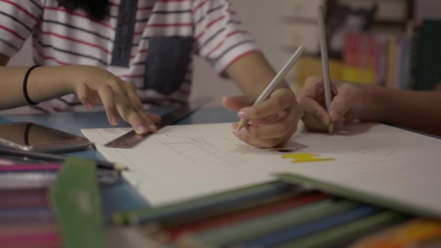 Two girls drawing on a paper and helping each other do homework on the desk at home. Education concept.