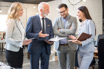 Mature and young businesswomen and businessmen standing in the modern office and analyzing business...