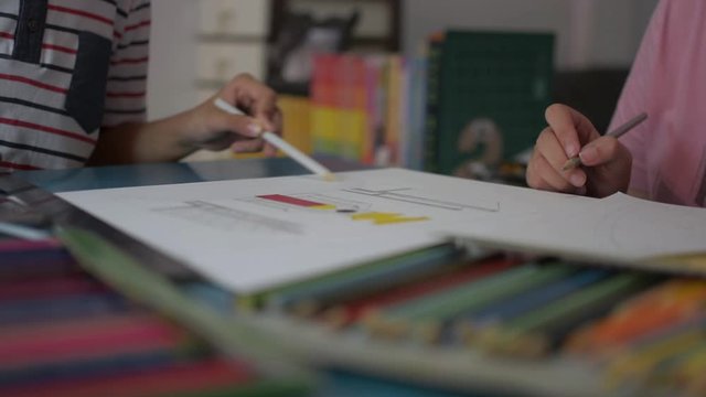 Two girls drawing on a paper and helping each other do homework on the desk at home. Education concept.