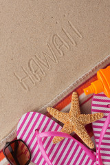Fototapeta na wymiar Word HAWAII written in sand with beach accessories.