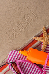 Fototapeta na wymiar Word DUBAI written in sand with beach accessories.