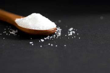 White sugar in wood spoon on black background