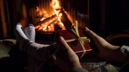 Woman holds a box with a gift in her hands, sits near the fireplace