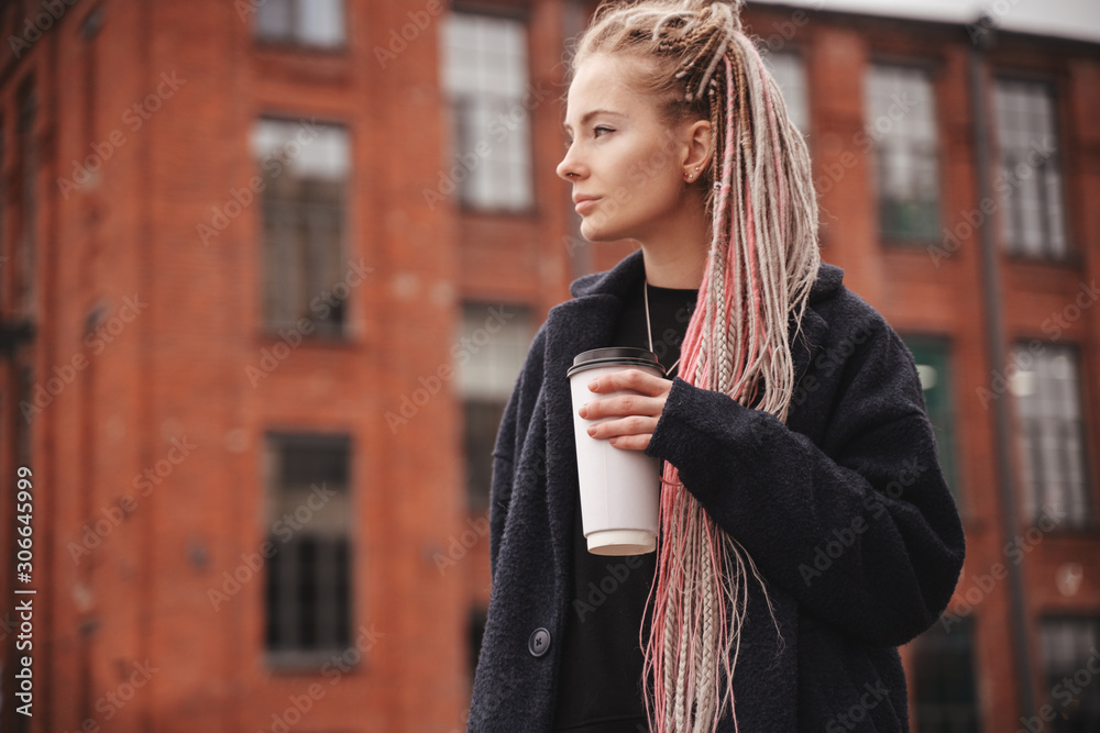 Wall mural stylish beautiful young blonde girl with pink dreadlocks with a white glass of take-away coffee, clo