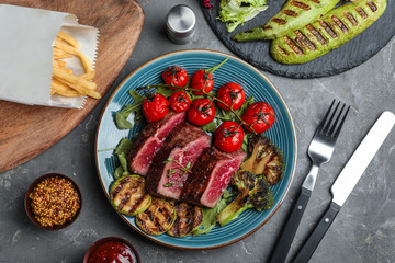 Delicious sliced beef steak served on grey table, flat lay