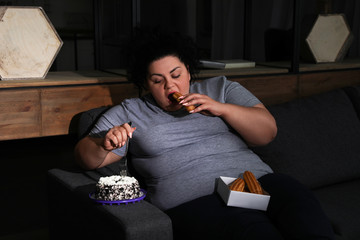 Depressed overweight woman eating sweets in living room at night