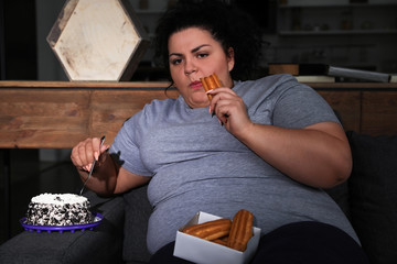 Depressed overweight woman eating sweets in living room at night