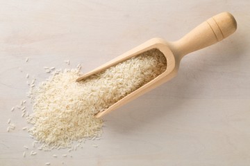 White uncooked, raw long grain rice in wooden scoop on white wooden table top view flat lay from above