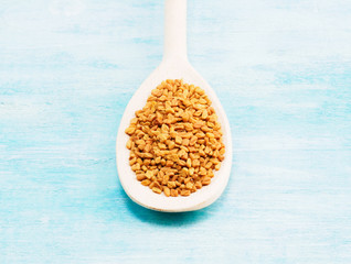 Fenugreek in wooden spoon on a blue background. Indian cuisine, ayurveda, naturopathy, modern apothecary concept