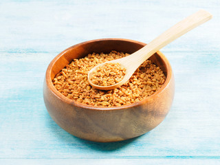 Fenugreek in wooden bowl and spoon on a blue background. Indian cuisine, ayurveda, naturopathy, modern apothecary concept