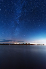 A magical starry night on the river bank with a milky way in the sky and falling stars in the winter.