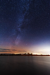 A magical starry night on the river bank with a milky way in the sky and falling stars in the winter.