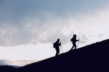 Two hikers silhouettes goes uphill in mountains