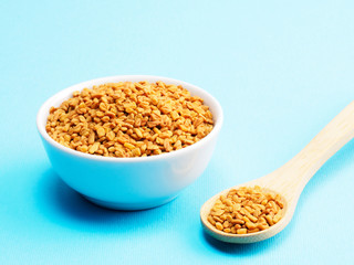Fenugreek in bowl and spoon on a blue background. Indian cuisine, ayurveda, naturopathy, modern apothecary concept