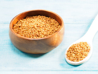 Fenugreek in wooden bowl and spoon on a blue background. Indian cuisine, ayurveda, naturopathy, modern apothecary concept