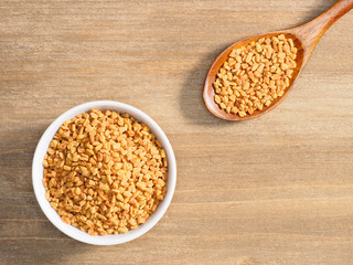 Fenugreek in white bowl and spoon on a brown wooden background. Indian cuisine, ayurveda, naturopathy, modern apothecary concept