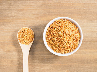 Fenugreek in white bowl and spoon on a brown wooden background. Indian cuisine, ayurveda, naturopathy, modern apothecary concept