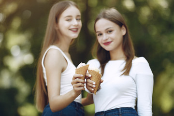 Beautiful girls in a jeans skirts. Women in a summer park. Friends with ice cream