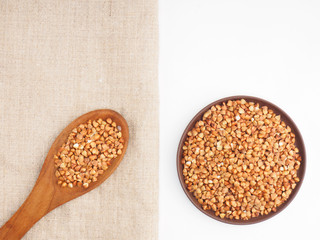 Buckwheat groats in clay plate and in wooden spoon on gray fabric and white background. Weight loss concept