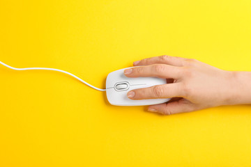 Woman using modern wired optical mouse on yellow background, top view