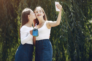 Obraz premium Beautiful girls in a jeans skirts. Women in a summer park. Friends with cocktails
