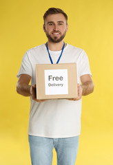 Male courier holding parcel with sticker Free Delivery on yellow background