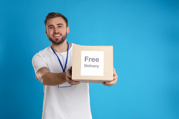 Male courier holding parcel with sticker Free Delivery on light blue background
