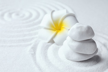 Fototapeta na wymiar Stack of white stones and beautiful flower on sand with pattern. Zen, meditation, harmony
