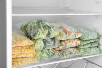 Plastic bags with different frozen vegetables in refrigerator
