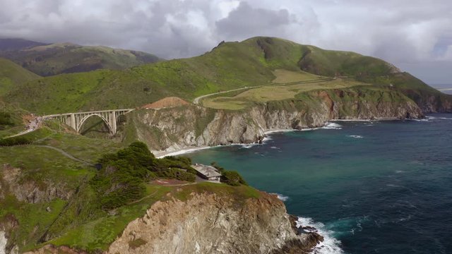 Breathtaking distant view over the famous beautiful landmark, Bixby Bridge. The arch bridge on the Big Sur coast of California. Lots of cars are seen on the view point and on the way to the bridge. 4k