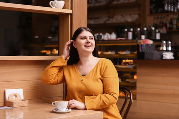 Beautiful overweight woman at table in cafe. Plus size model