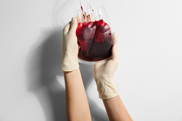 Woman holding blood for transfusion on light background, closeup. Donation concept