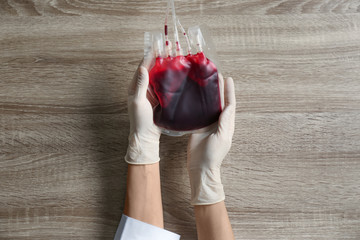 Woman holding blood for transfusion at wooden table, top view. Donation concept