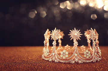 low key image of beautiful queen/king crown over gold glitter table. vintage filtered. fantasy medieval period