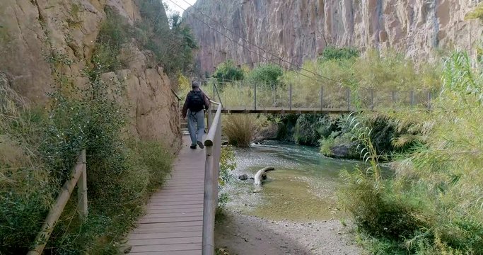 Escursionista senior sobre puente colgante y dron le sigue por detr&aacute;s