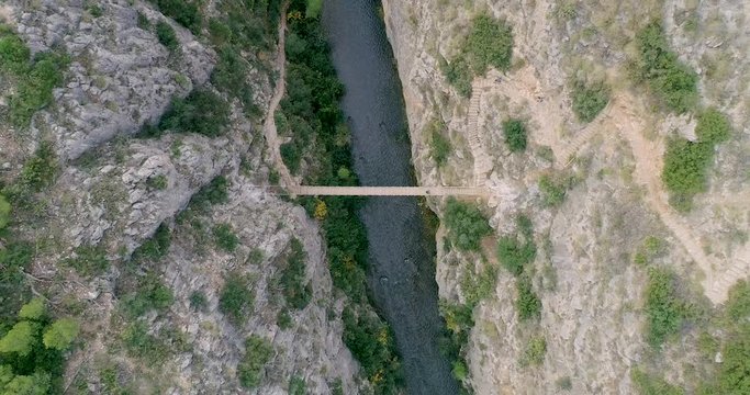 Descenso cenital de dron hacia barranco profundo y al fondo puente colgante
