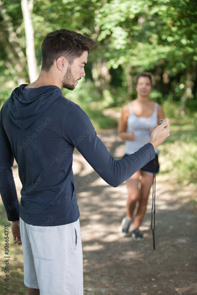 Wall mural Female runner approaching man holding stopwatch