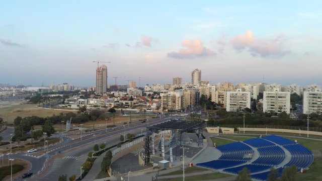 Aerial flying over an Ashdod city and Ashdod-Yam Park with cloudy sunset sky, buildings, sea and coast at the background. View from above of Ashdod, Israel