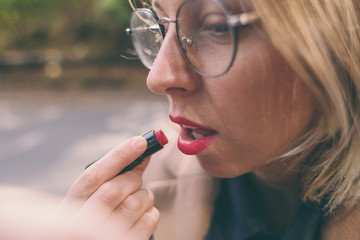 Woman paints her lips with red lipstick.