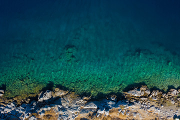 Aerial view to clear blue green sea with rocks, beautiful nature background. Greek island