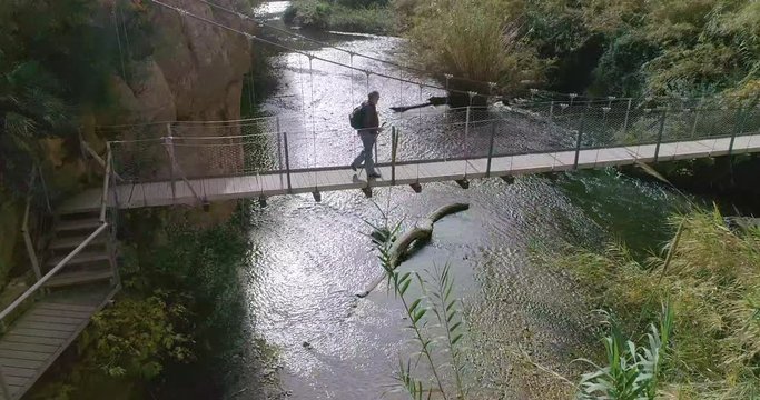 Senior cruzando un rio sobre puente colgante y el dron se desplaza lateralmente