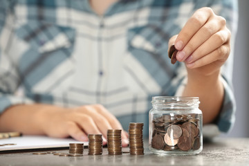 Fototapeta na wymiar Woman putting money into glass jar at table, closeup