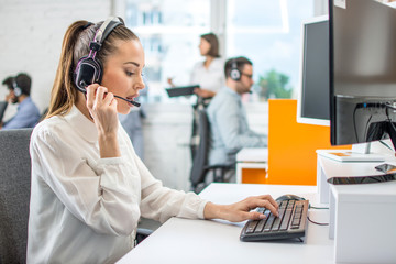 Beautiful female call center operator working on computer in office