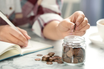 Woman putting money into glass jar at white marble table, closeup