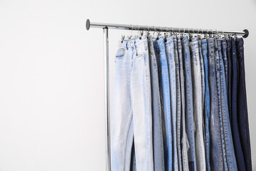 Rack with different jeans on light background. Space for text