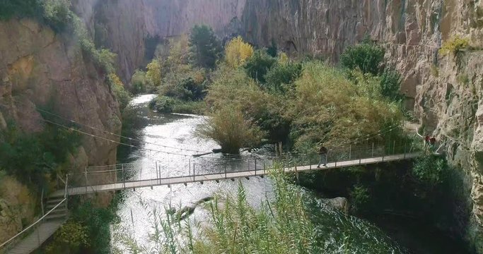 Anciano senderista de barba canosa cruza un puente colgante de r&iacute;o dentro de barranco