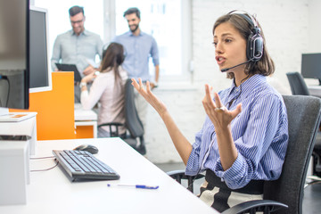 Confused young call center worker shrugging shoulders and looking at computer screen in office