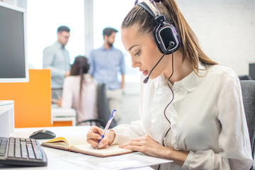 Customer support operator woman talking to a client and writing notes to notebook in call center