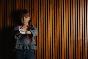 Sad little girl with sign HELP on wooden background, space for text. Child in danger