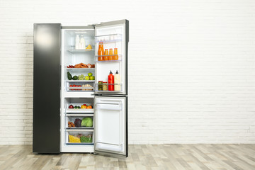 Open refrigerator filled with food near white brick wall, space for text